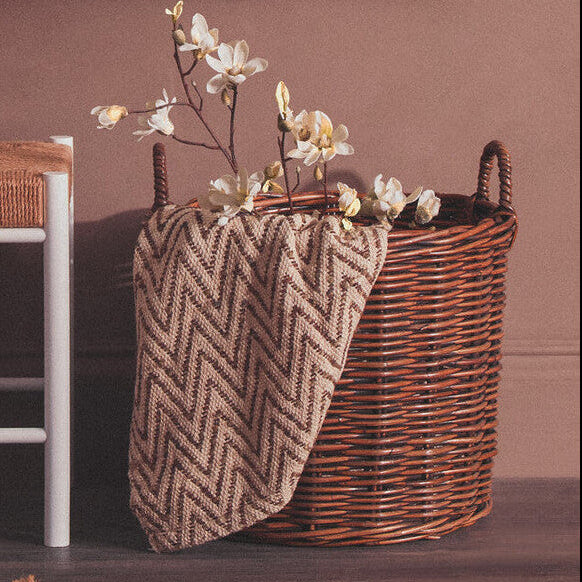 Wicker basket with flowers and a patterned cloth against a brown wall.