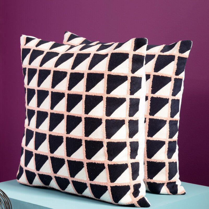 Two geometric-patterned pillows on a teal surface with a purple background