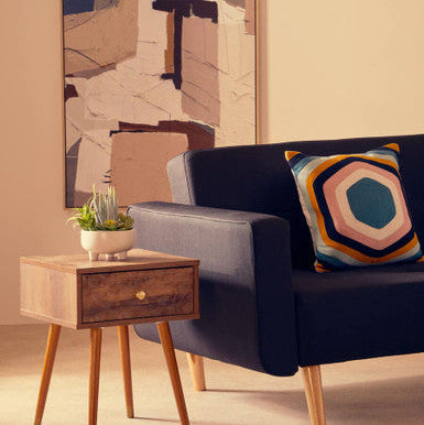 Navy blue sofa with a colorful pillow next to a wooden side table in a living room setting.