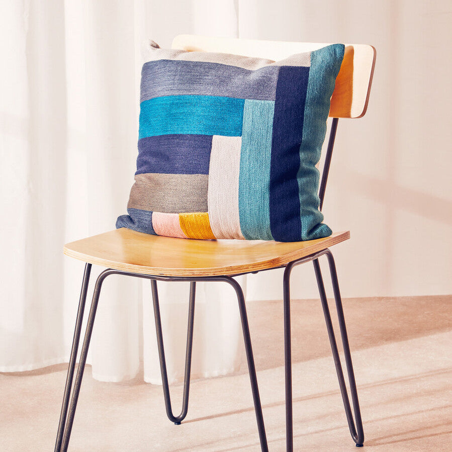 Colorful patchwork pillow on a wooden chair with a light background