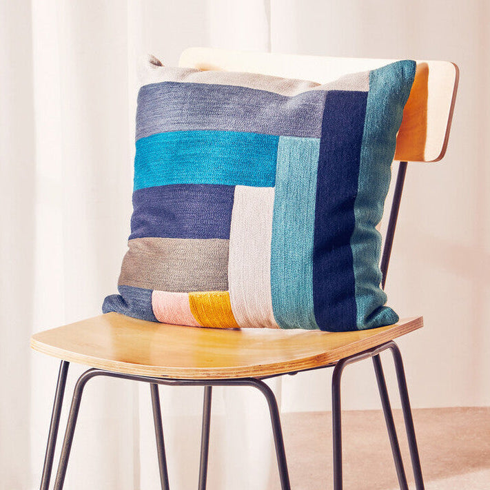 Colorful patchwork pillow on a wooden chair with a light background