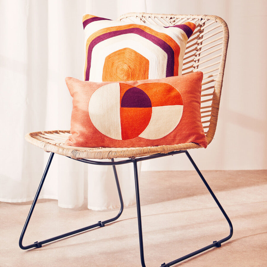 Woven chair with colorful geometric cushions against a white curtain background