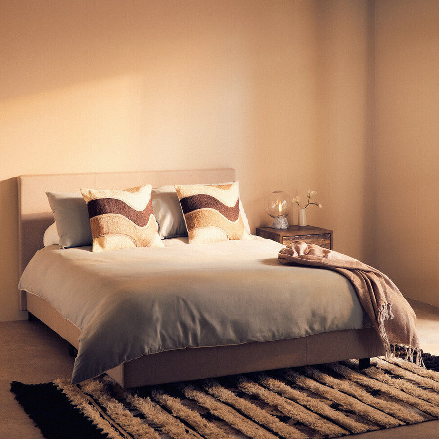 Neatly made bed with decorative pillows and a blanket in a softly lit bedroom.