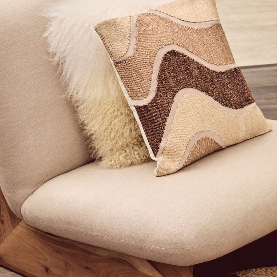 Decorative pillow on a beige sofa with wooden armrests.