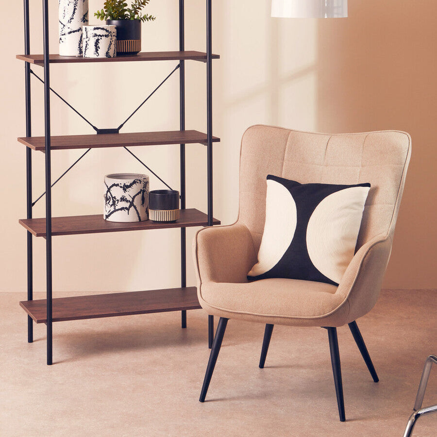 Beige armchair with a decorative pillow next to a wooden shelf against a beige wall.