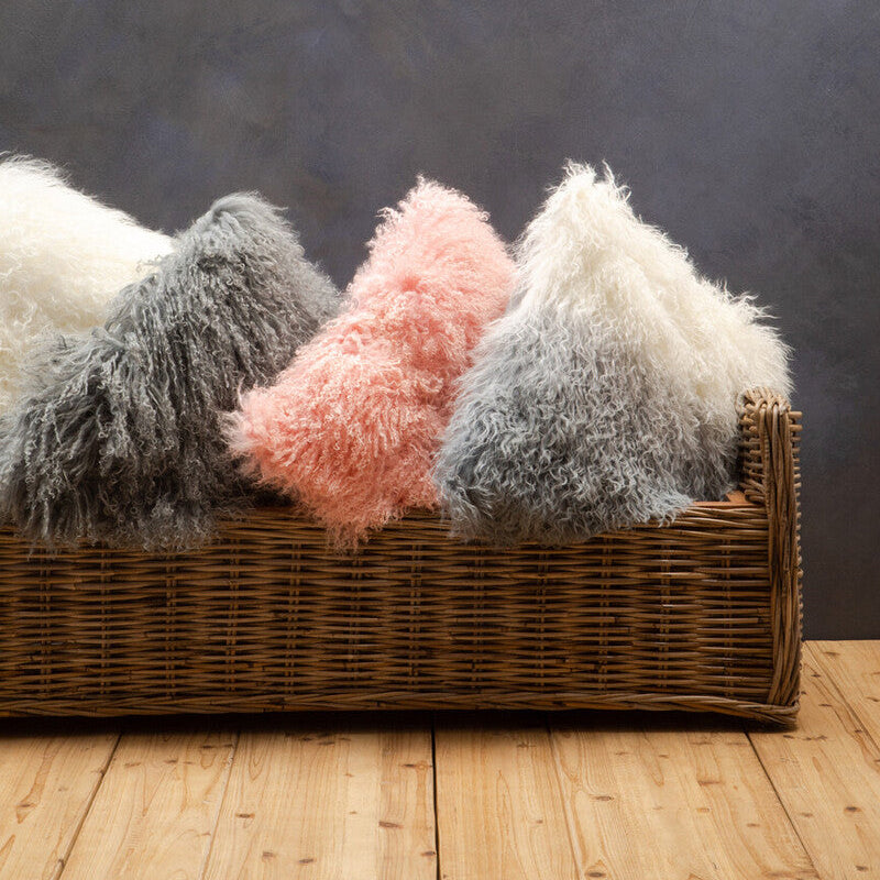 Wicker basket with fluffy textured pillows on a wooden floor against a dark wall.