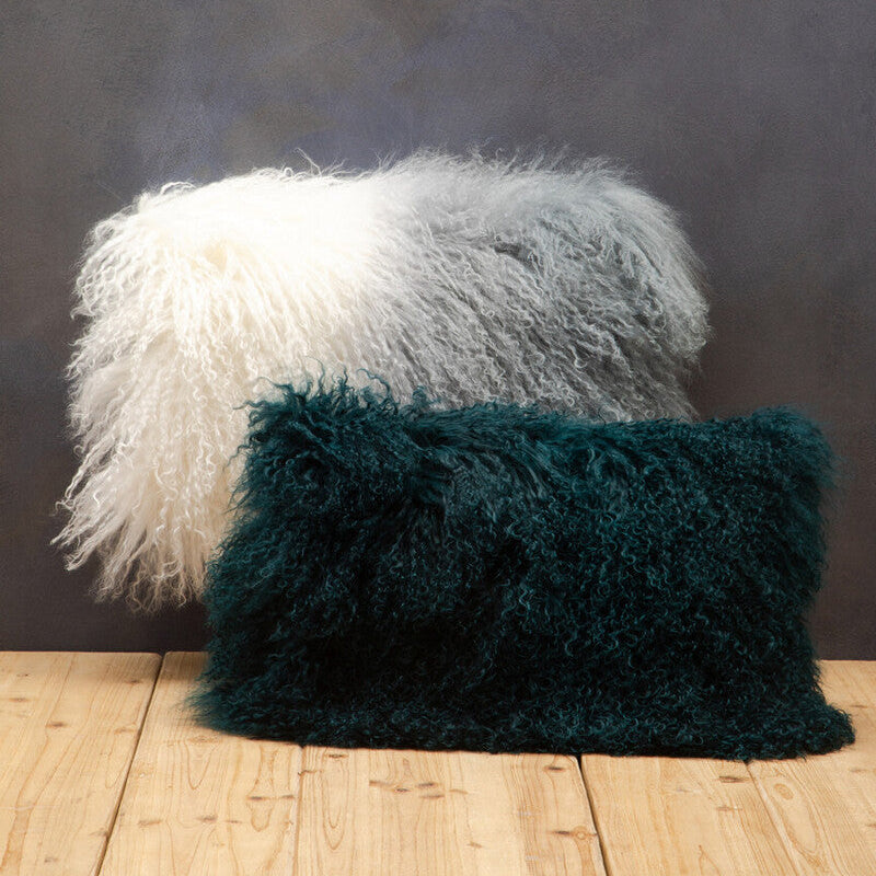 Two fluffy pillows, one white and one green, on a wooden floor against a dark wall.