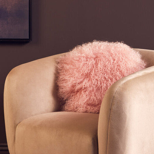 Beige armchair with a pink fluffy pillow against a dark wall.