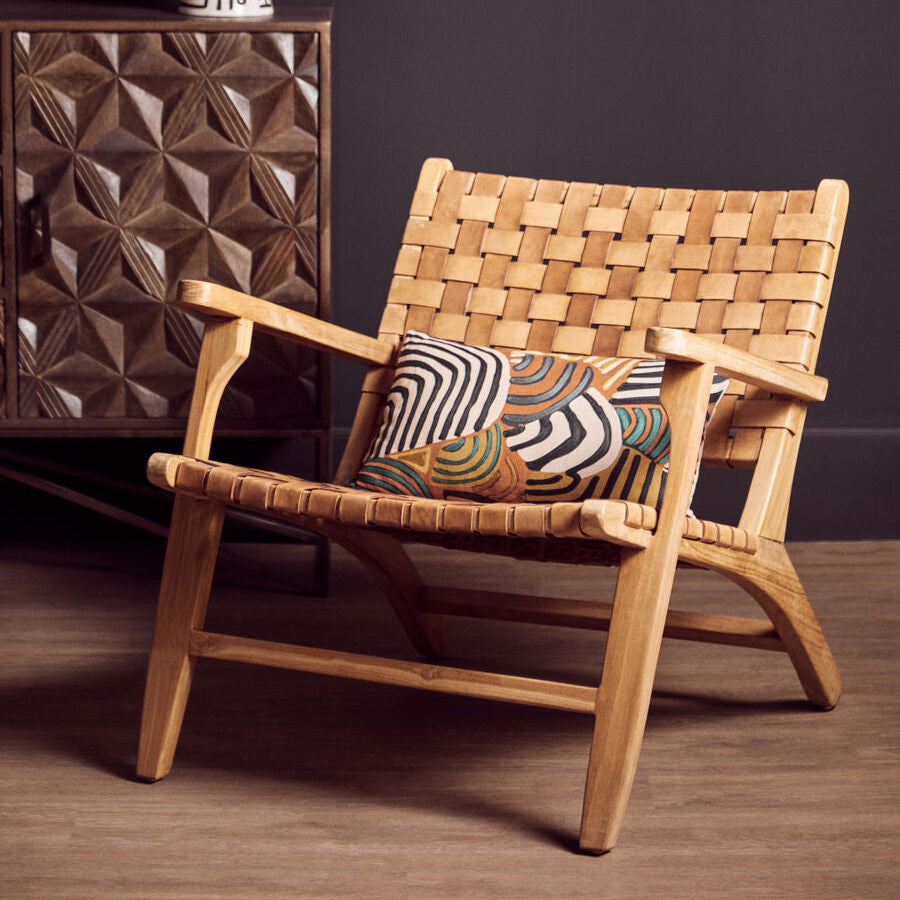 Woven wooden chair with a patterned cushion against a dark wall.