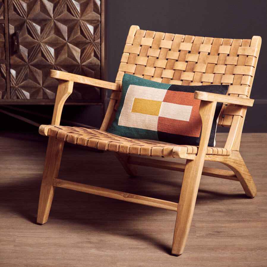 Woven wooden chair with a colorful pillow against a dark wall.