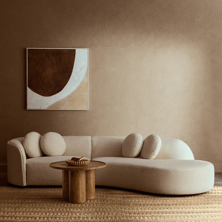 Modern living room with a beige sofa, wooden coffee table, and abstract art on a brown wall.