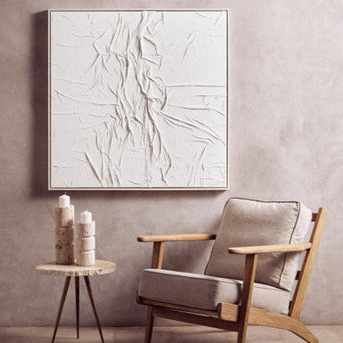 Modern armchair with a side table and abstract artwork in a minimalistic room.