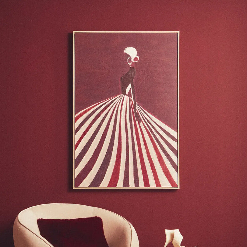 Modern beige armchair with a red pillow in a room with a red wall and a framed artwork.
