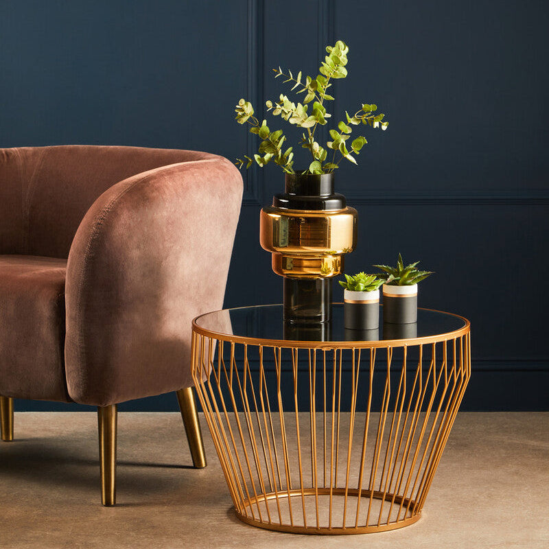 Gold wire side table with decorative items next to a brown armchair against a dark blue wall.