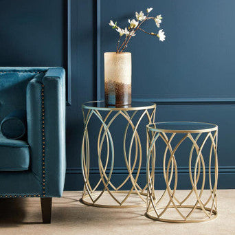 Gold side tables with a vase and branch against a blue wall
