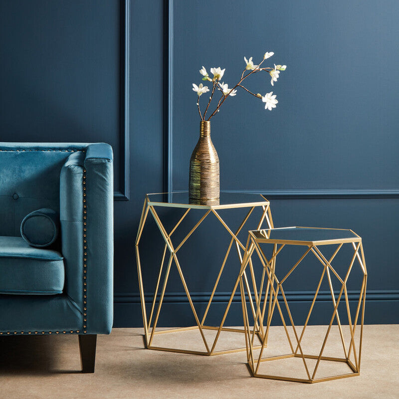 Gold geometric side tables with a vase of flowers against a blue wall.