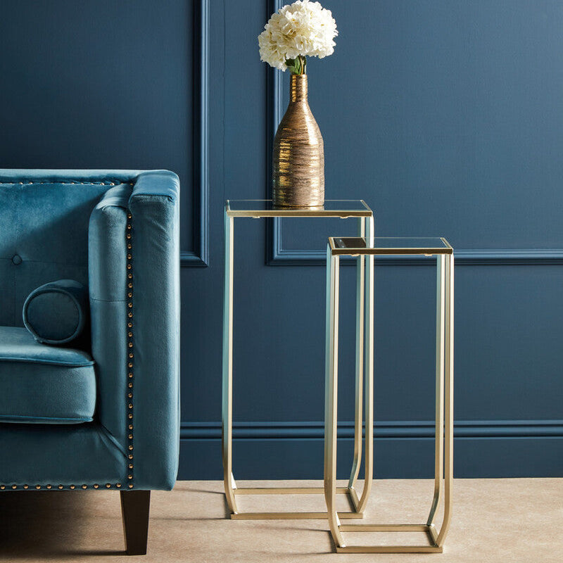 Gold side tables with a vase of white flowers against a blue wall.