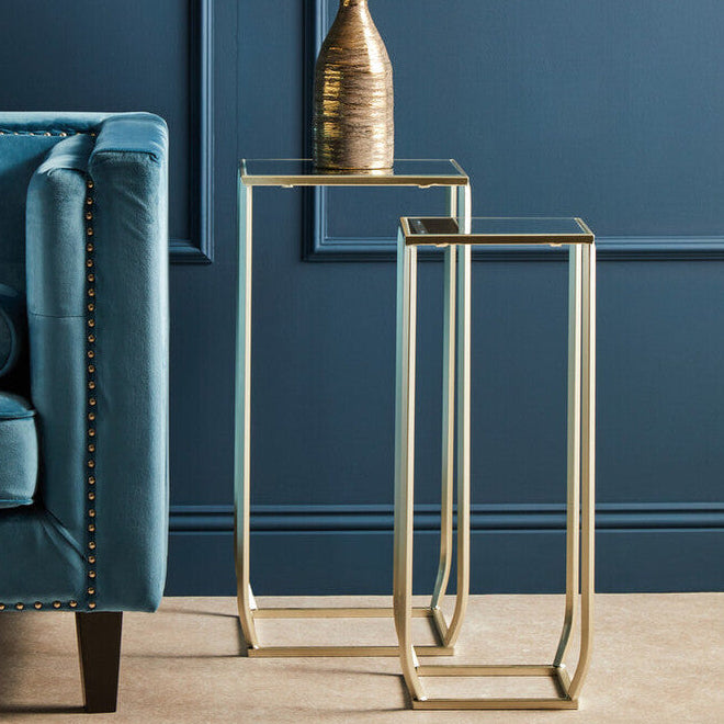Gold side tables with a vase of white flowers against a blue wall.