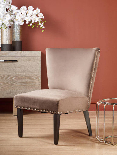 Beige upholstered chair with nailhead trim in a room with a wooden floor and red wall.