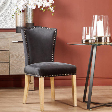 Black upholstered chair with wooden legs in a room setting with a table and decorative elements.