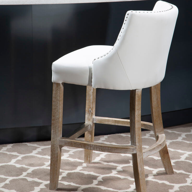 White bar stool with wooden legs in front of a dark wall and light gray countertop.