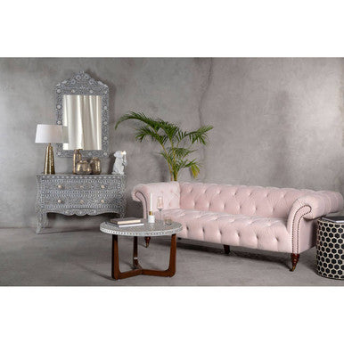 Pink sofa in a room with decorative mirror and table.