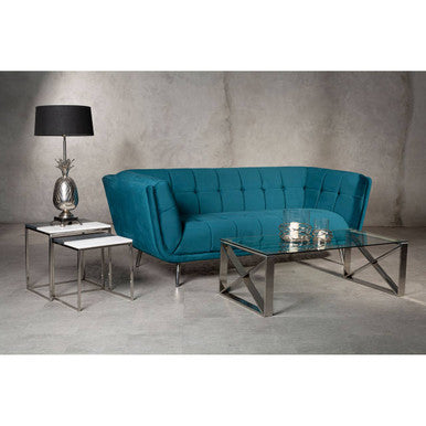 Modern living room setup with a blue sofa, glass coffee table, and lamp against a concrete wall.