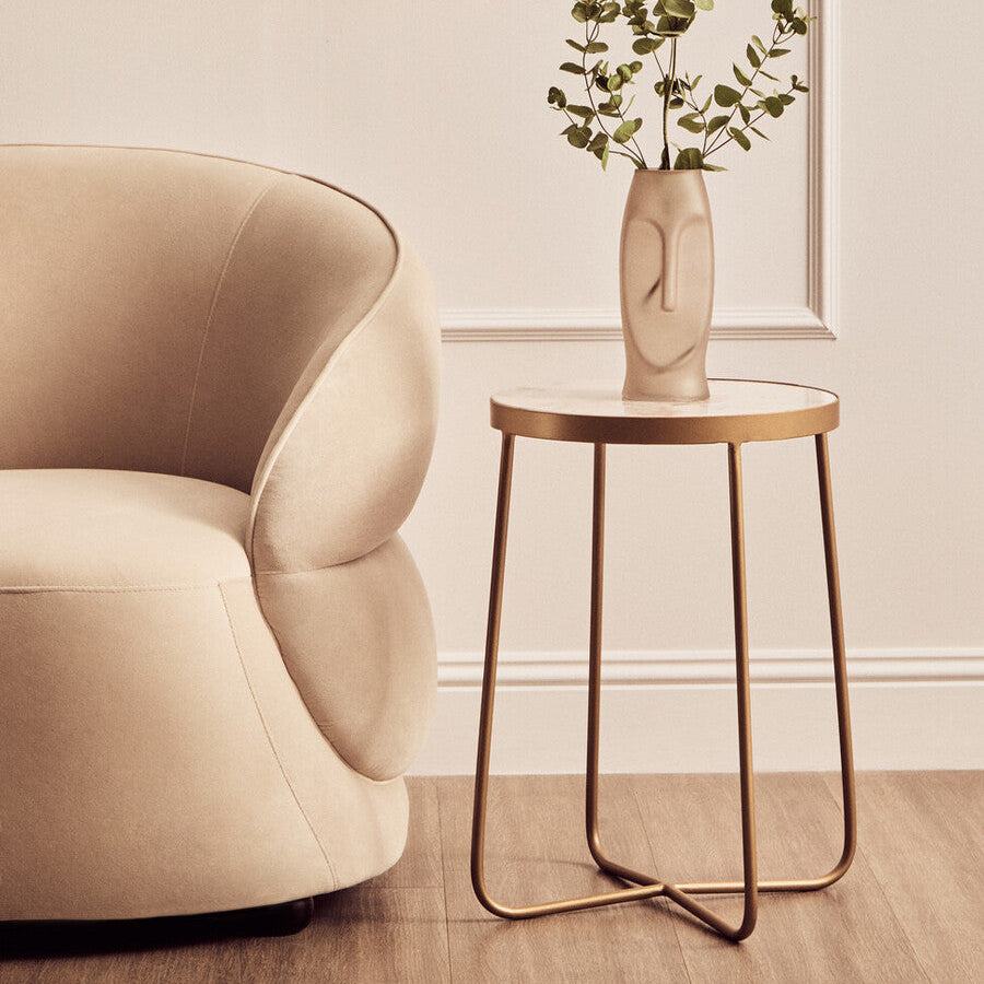 Beige armchair next to a small round table with a vase and plant in a room.