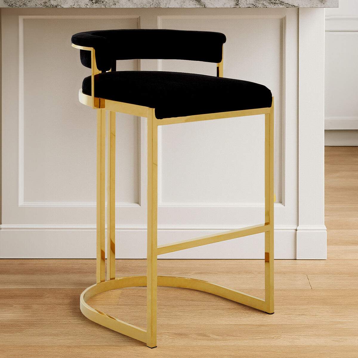 Black cushioned bar stool with gold frame on a wooden floor.