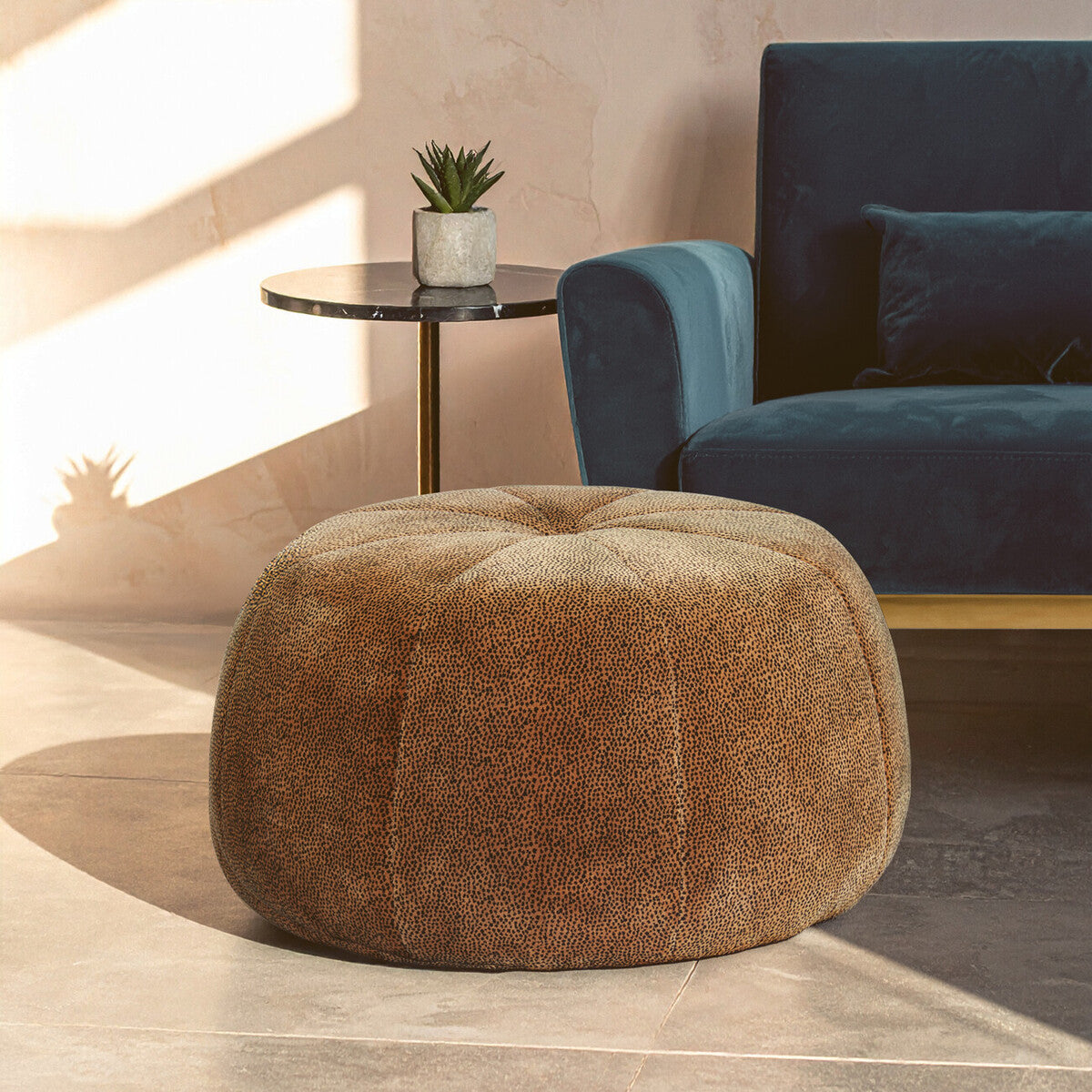 Brown textured ottoman in a living room setting with a blue sofa and small table.