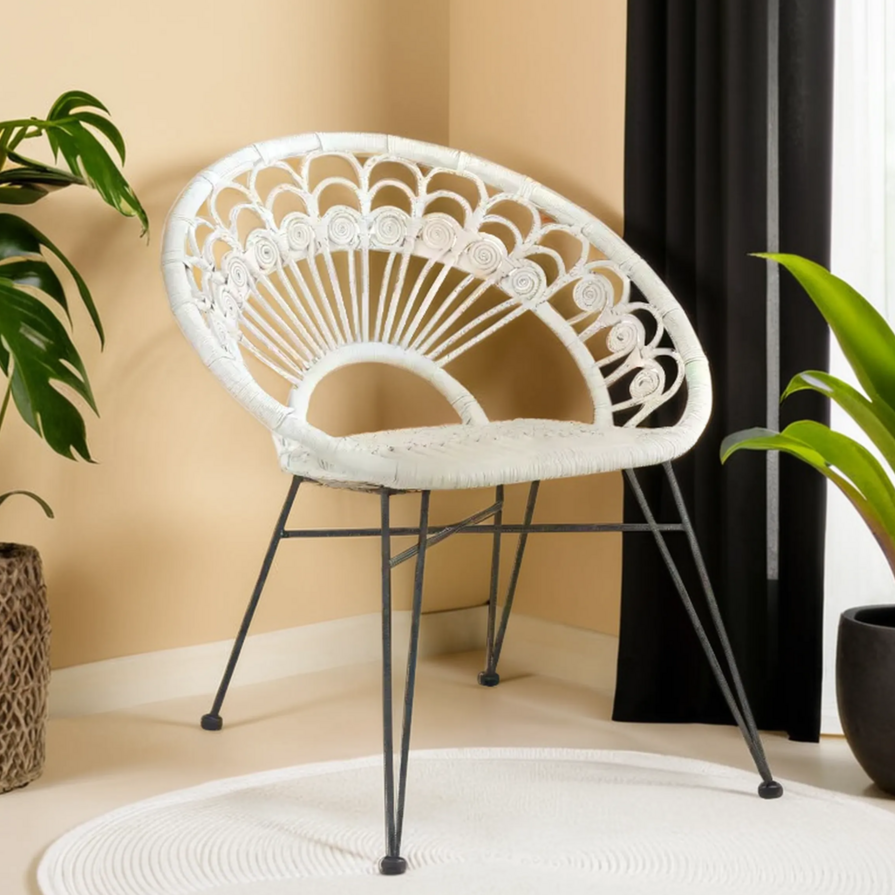 White wicker chair with black metal legs in a room with plants and curtains.
