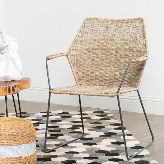 Wicker chair and ottoman on a checkered rug with a plant and small table in the background.