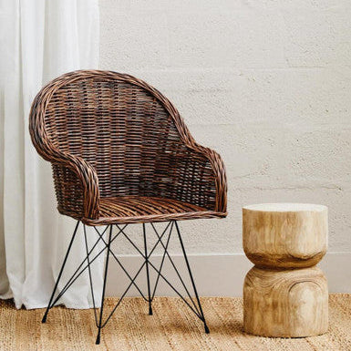 Wicker chair with metal legs next to a wooden stool against a light-colored wall.