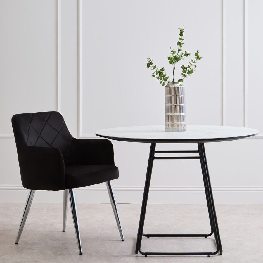 Black chair and round table with a vase of greenery against a white wall.