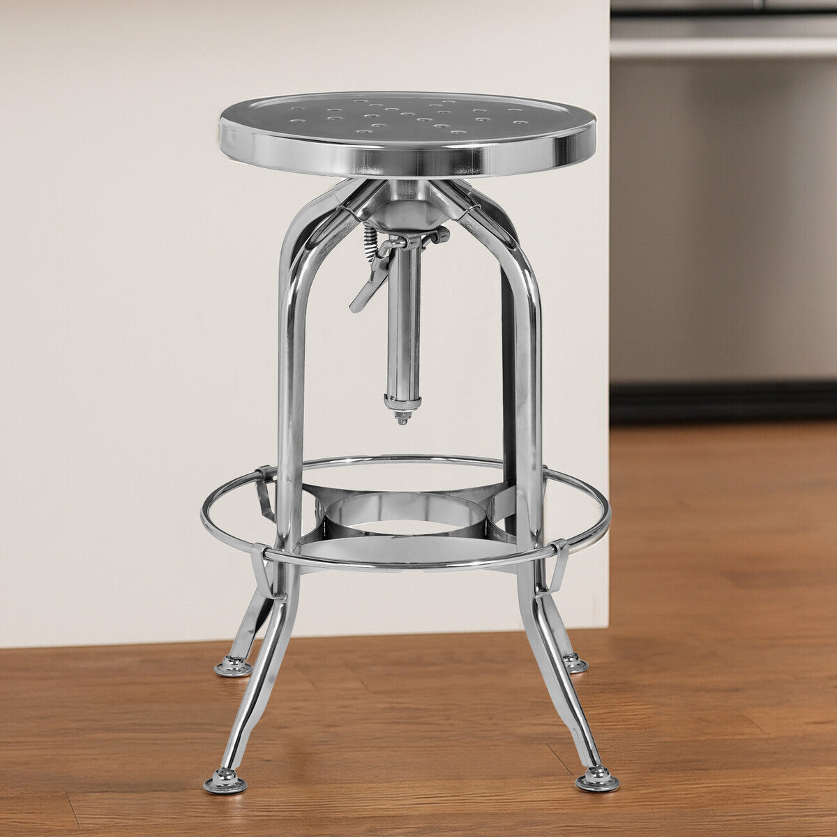 Chrome bar stool with round seat and adjustable height mechanism on a wooden floor.