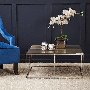 Modern interior with a blue armchair, silver coffee table, and white orchids against a dark wall.