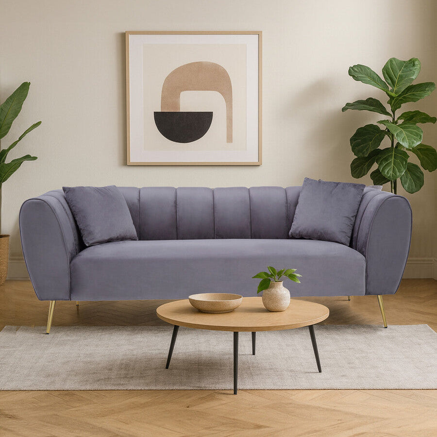 Gray sofa in a living room with a round wooden coffee table, plants, and abstract art on the wall.
