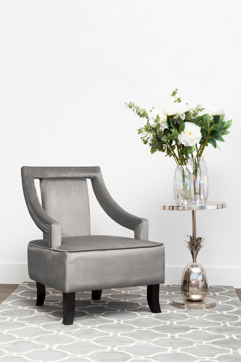 Gray velvet armchair with a small round table and vase of flowers on a patterned rug.