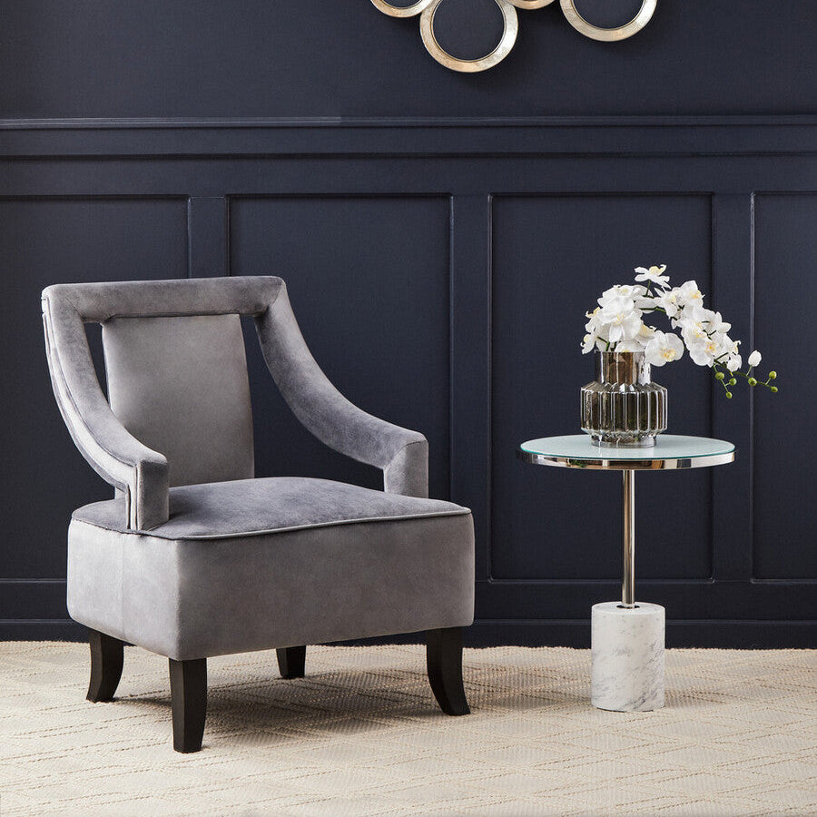 Gray velvet armchair in a room with decorative wall art and a small table with flowers.