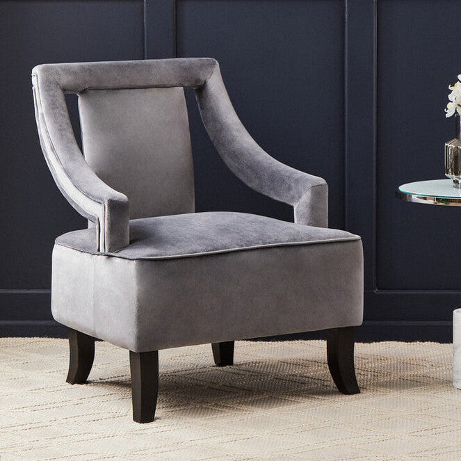 Gray velvet armchair in a room with decorative wall art and a small table with flowers.