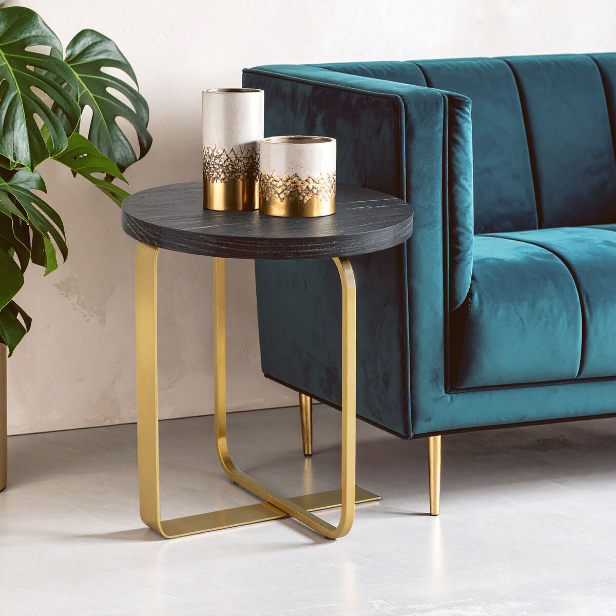 Teal sofa with a small round table featuring gold legs and two decorative cylindrical vases.