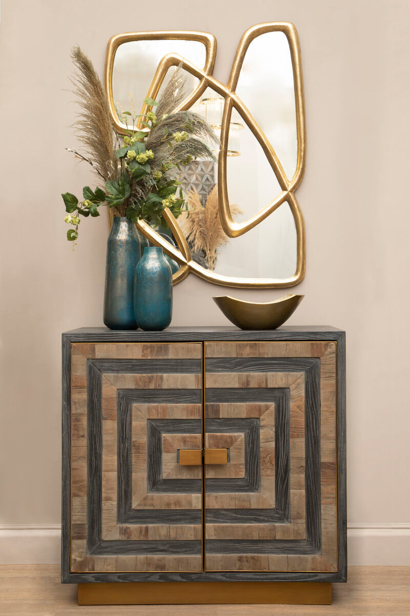 Decorative cabinet with geometric design, gold accents, and a mirror above it on a beige wall.