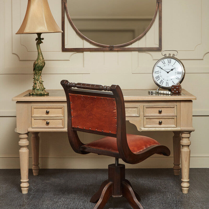 Vintage-style desk with leather chair, round mirror, and lamp against a beige wall.