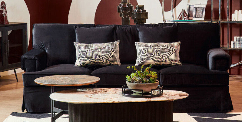 Modern living room with black sofa, round coffee table, and abstract wall design.