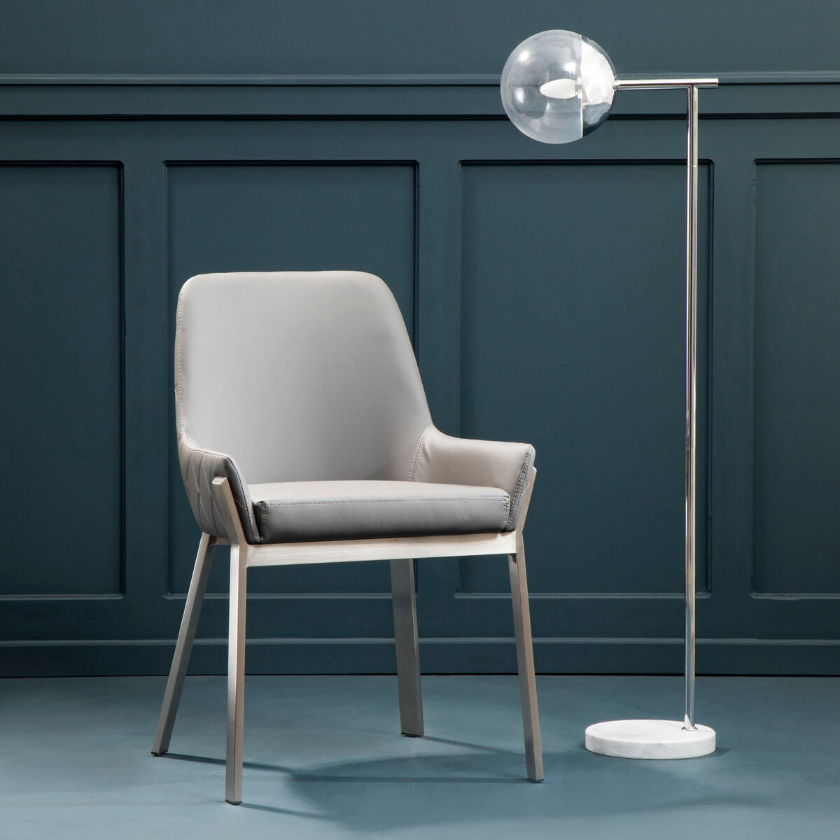 Gray chair and modern floor lamp against a dark paneled wall.