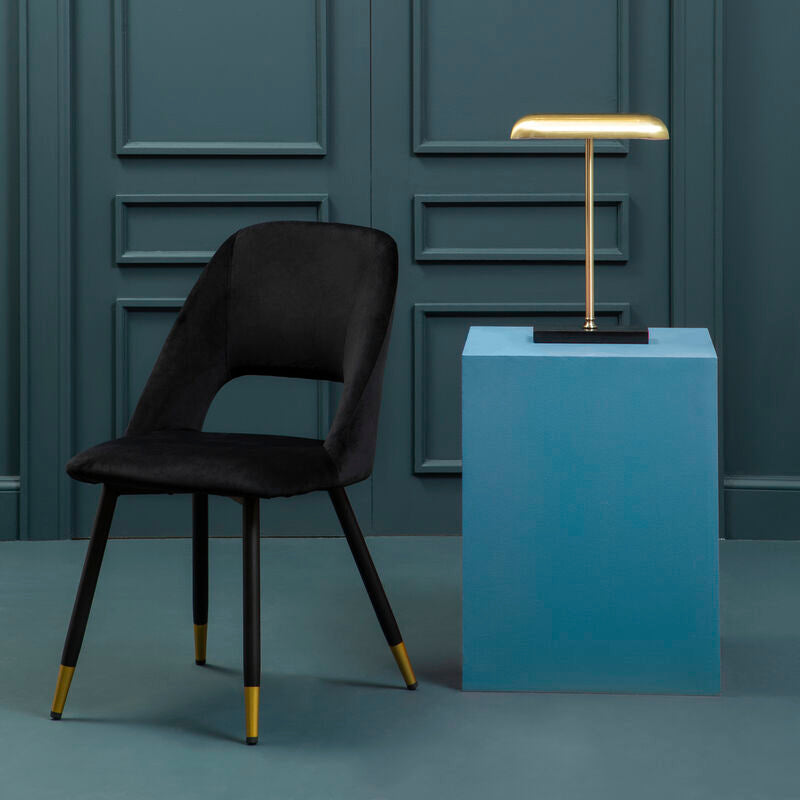 Black chair and gold lamp on a blue pedestal against a gray paneled wall.