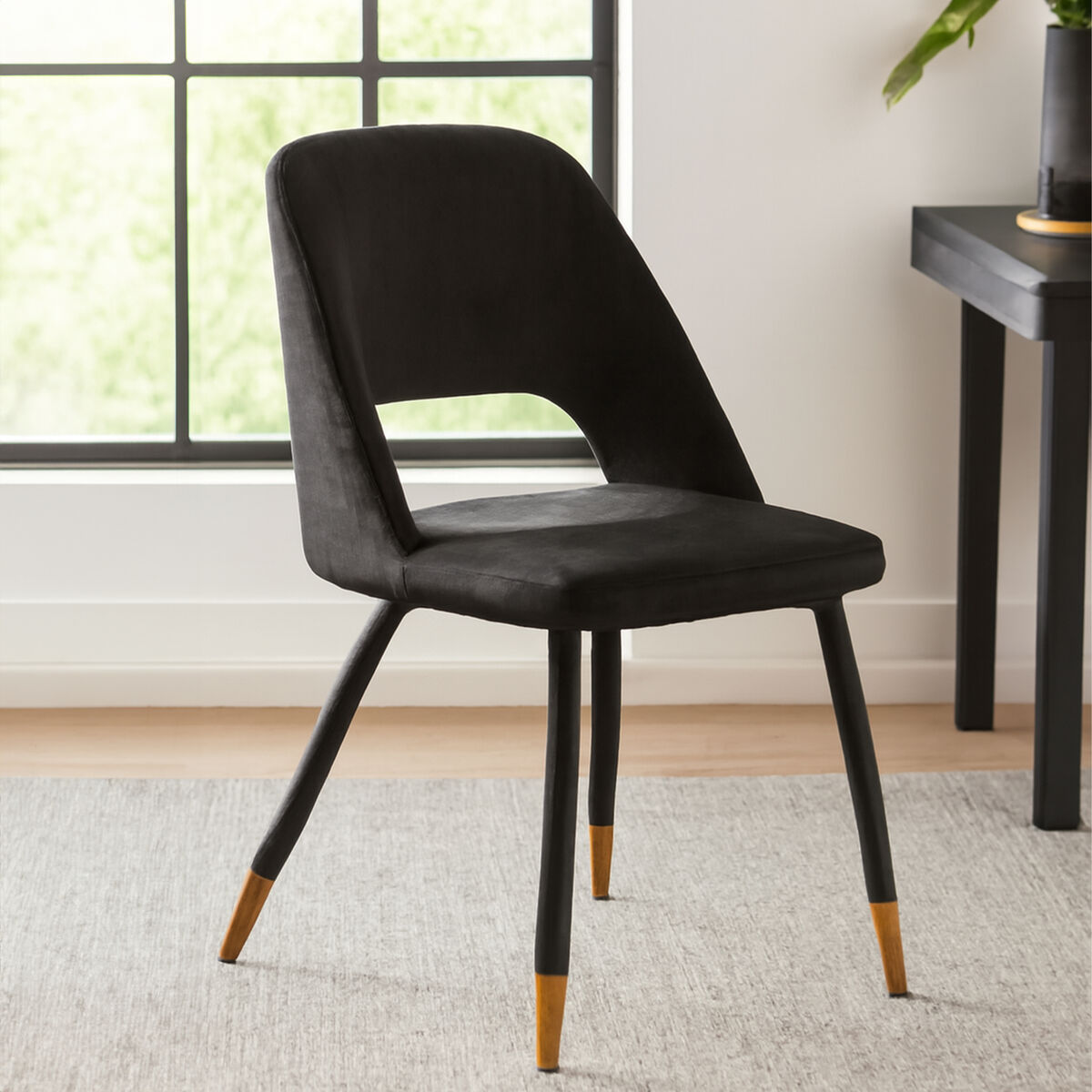 Black chair with gold accents on a gray rug in a room with a window and desk.