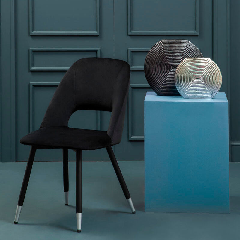 Black chair and decorative items on a blue pedestal against a gray wall.