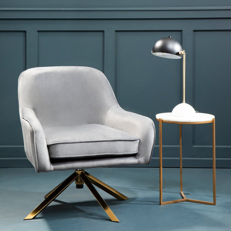 Gray armchair with gold base next to a small table with a lamp against a blue wall.