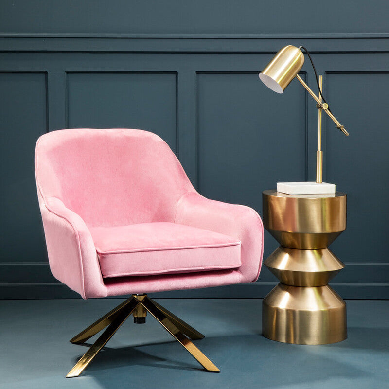 Pink armchair with gold base and a matching lamp on a blue floor against a dark blue wall.